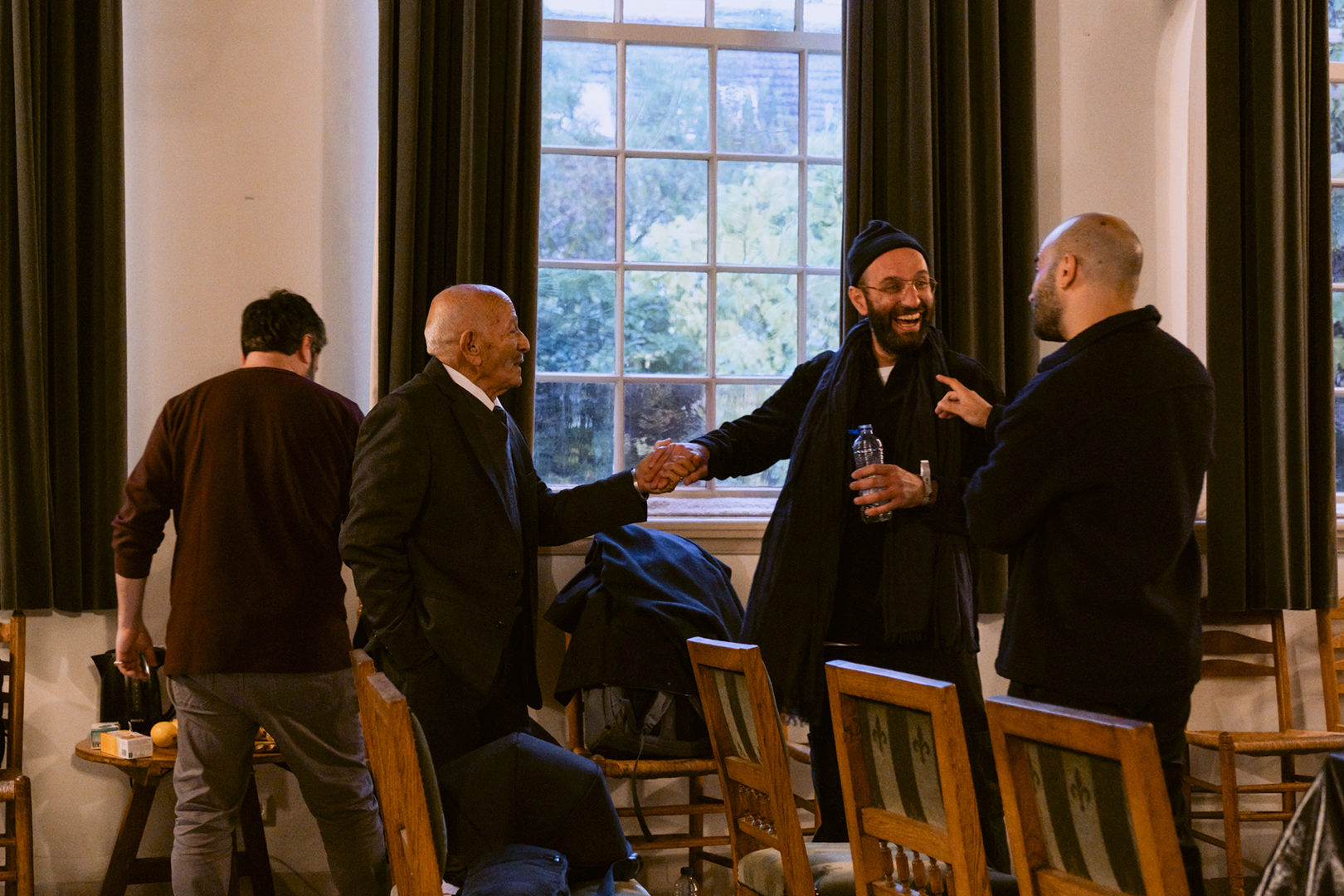 The photo shows four men. Three are talking to each other and laughing while two are holding hands.